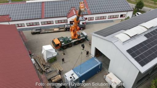 Luftaufnahme eines Containers, der mit einem Kran aus einer Halle mit PV-Modulen heraus entladen wird.