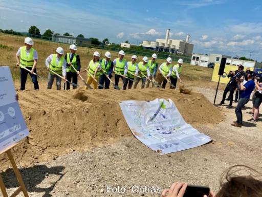 Männer mit gelben Warnwesten und Helmen und Schaufeln stehen hinter Erdwall, auf dem ein Banner liegt, Fotografen - Baustart für das Wasserstoff-Startnetz