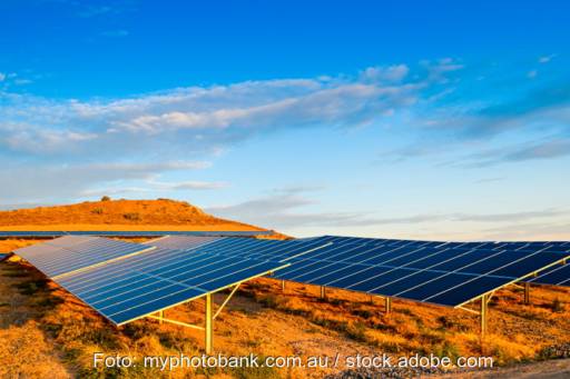 Aufgeständerte Solarpanels über rotrer Erde bei blauem Himmel.