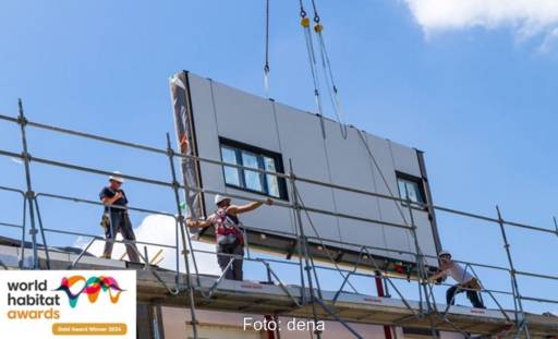 Ein Fassadenelement mit Fensteröffnung wird an einem Kran zu einem Haus heruntergelassen - Serielle Sanierung.