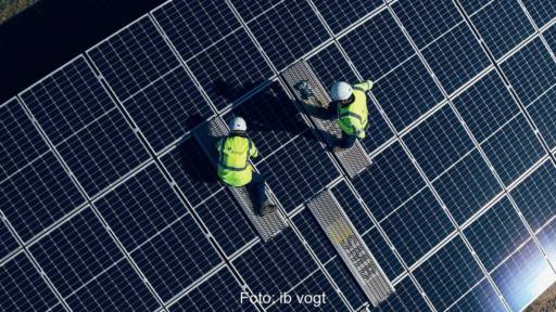 Zwei Menschen in gelben Westen und mit Helm montieren Solarmodule - Symbolbild für Photovoltaik- und Batterieprojekt in Großbritannien.