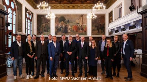 Zwölf weiße Männer und vier weiße Frauen in dunklen Anzügen in einem Festsaal - Energieminister-Konferenz in Merseburg.