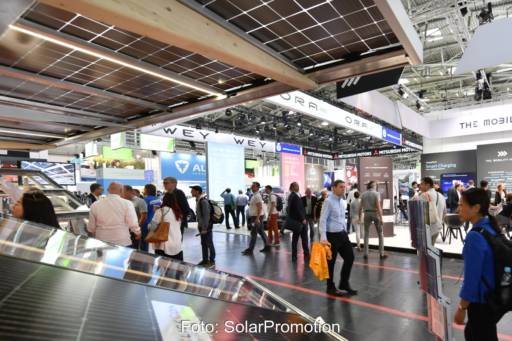 Passanten auf einer Messe mit Automobilständen und Photovoltaik.