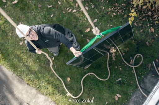 Ein Solarmodul wird per Flaschenzug transportiert, ein Mann mit Schutzhelm kontrolliert den Vorgang.