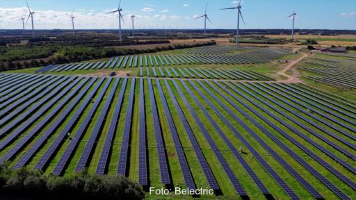 Luftbild einer Photovoltaik-Freiflächen-Anlage, im Hintergrund Windräder