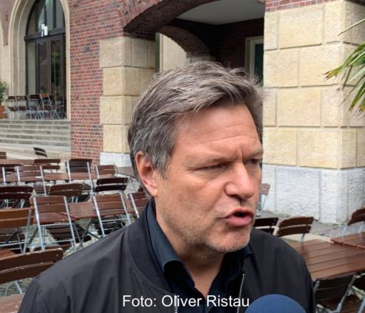 Portrait des Bundesministers Robert Habeck auf einer Terrasse mit Tischen und Stühlen.