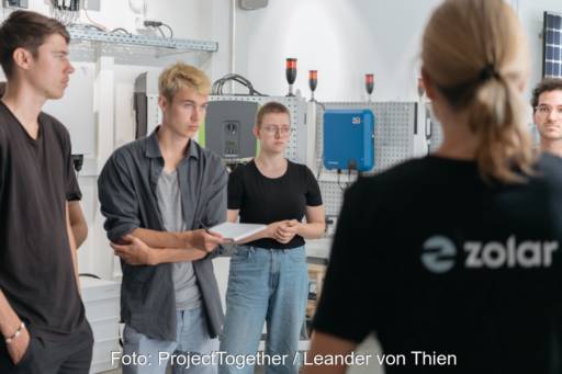 Mehrere junge Menschen stehen im Kreis in einem Raum mit technischen Geräten - Schulung für Photovoltaik-Hilfskräfte.
