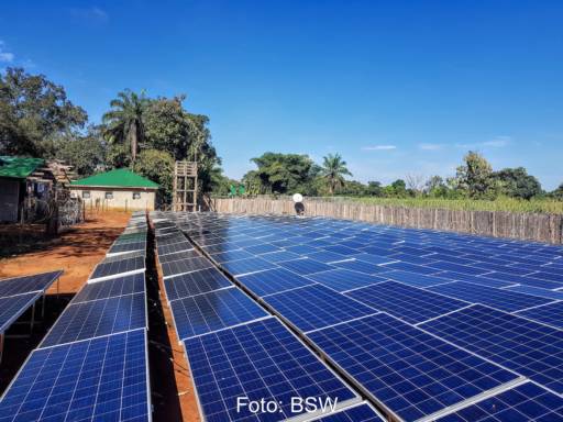 Photovoltaik-Anlage vor dunkelblauem Himmel auf rotem Boden, wenige Bäume - Solarstrom in Afrika.