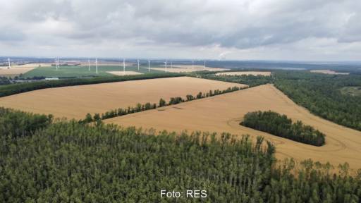 Luftbild einer Acker-Fläche, im Hintergrund Windenergie-Anlagen - hier soll der neue Solarpark entstehen.