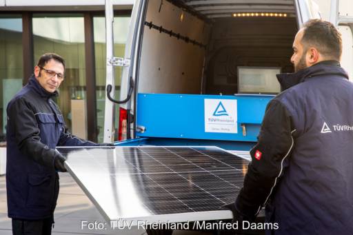 Zwei Männer heben PV-Modul in mobiles Prüflabor für Test