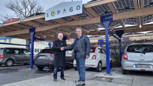 Zwei Männer stehen vor Solar-Carport auf Parkplatz und schütteln sich die Hand.