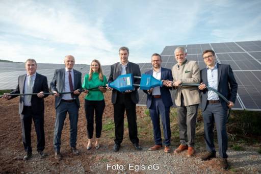 Sechs Männer und eine Frau halten ein dickes Kabel mit einem symbolischen Stecker - Inbetriebnahme am Solarpark Bundorf.