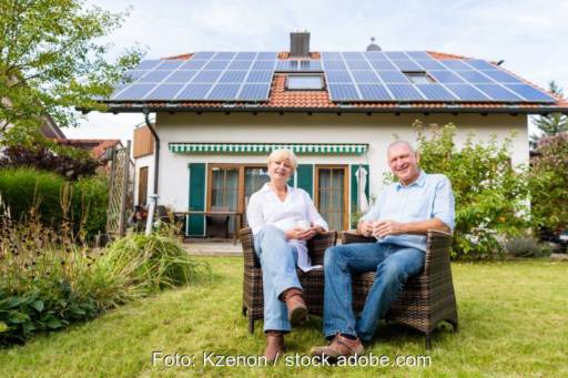 Älteres Paar zufrieden im Garten vor Haus mit PV-Anlage.