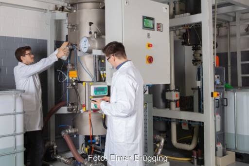 Zwei Männer in weißen Kitteln an einer Biogas-Anlage mit Hochlastfermenter.