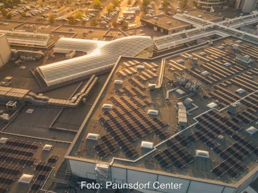 Luftbild zeigt Photovoltaik-Anlage auf Dach des Shoppingcenters bei schräg stehender Sonne.