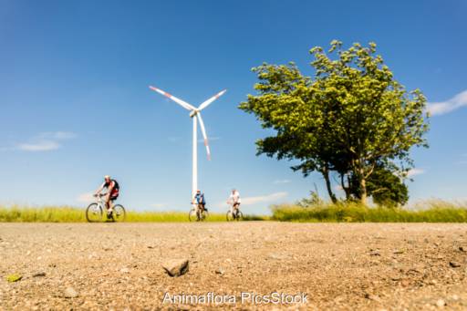 Drei Menschen auf dem Fahrrad fahren vor einer Windenergie-Anlage vorbei - Symbolbild für die Energiewende-Radtour