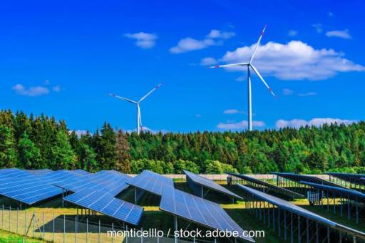 Ein Solarpark neben einem Wald und Windenergieanlagen.