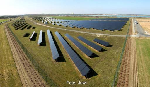 Ein Freiflächensolarpark im Flachland am Rande eines kleinen Binnengewässers.