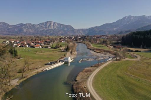 Blick auf einen Fluss mit neuem Wasserkraftwerk vor der Kulisse der Alpen.