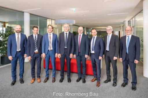 Acht Herren in Anzügen in einem Büro vor der Kamera.